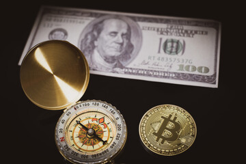 a bitcoin coin lies next to a compass and a hundred dollar bill