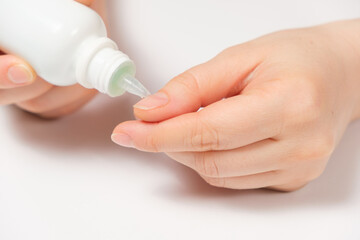 Woman applies cuticle remover to nails on white background