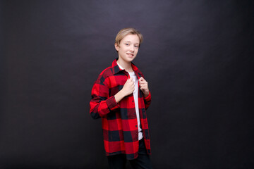 Smiling toothy funny young caucasian teenage guy in simple casual t-shirt and shirt in red cage looking at camera, isolated on studio portrait against black wall background. Emotions lifestyle concept