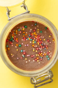 chocolate vegan ice cream in a glass jar with a lid on a yellow background. homemade ice cream with colored powder for decoration. delicious and sweet cold ice cream for dessert. natural dessert