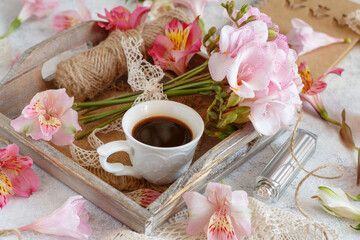 Coffee and pink flowers on a tray on white table