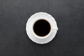 White cup of fresh black coffee on dark table background. Closeup. Top down view.