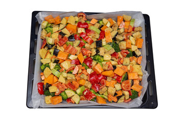 Finely chopped and seasoned vegetables on a baking sheet lined with baking paper isolated on white background. Potatoes, bell peppers, squash, pumpkin and broccoli. Vegetarian food, close-up