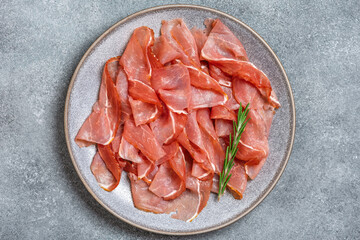 Close-up slices of prosciutto di parma or jamon serrano in a plate on gray grunge background. Top view, flat lay