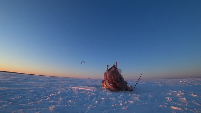 Homemade plastic tent on ice. A fisherman made a windbreak for ice fishing. A strong wind flutters, sways plastic. Frozen water, sea ice. Day. Winter. Russia.