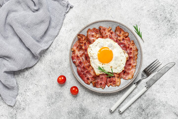 Fried egg with bacon on a plate, gray rustic background. Delicious appetizing breakfast. Top view, flat lay, copy space.