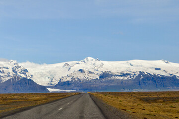 The long, straight road approaching the stunning, snow-capped mountains and glaciers of Skaftafell National Park. Taken on a sunny day with blue skies - Iceland