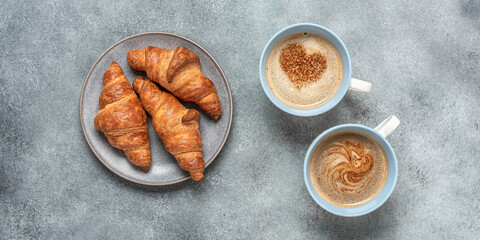 Cup of coffee with hearts and fresh croissants on gray grunge background. Top view, flat lay....