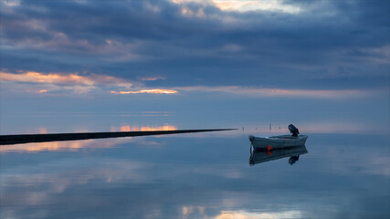 Barca a motore ferma, ormeggiata in riva al mare all'alba. Cielo coperto da nuvole con i primi raggi di sole.