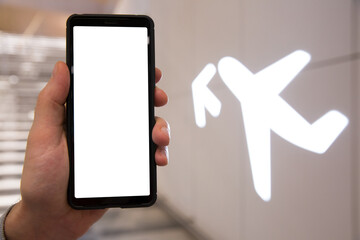 Smart phone with white screen in hand. Airport hall interior. Person traveling and using phone app. Departure gate on the background.