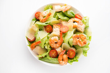 Caesar salad with fresh leaves, shrimp, cherry tomatoes in a plate isolated on a white background.