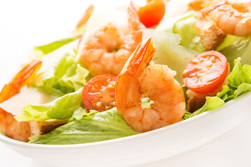 Caesar salad with fresh leaves, shrimp, cherry tomatoes in a plate isolated on a white background.