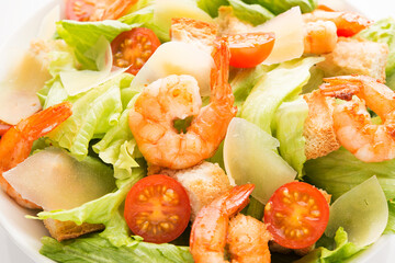 Caesar salad with fresh leaves, shrimp, cherry tomatoes in a plate isolated on a white background.