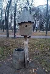 Decorative wooden birdhouse in the park and trash can near it