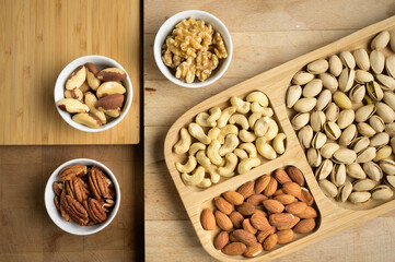 Different nuts and bowls closeup on a wooden table and brown background. Peanut, nut, cashew, almond, hazelnut, pistachio
