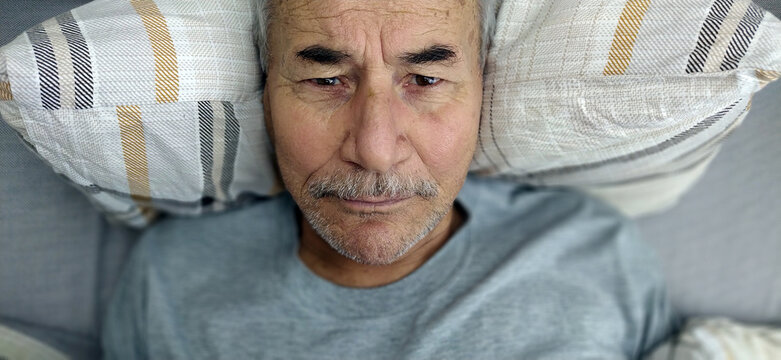 aged retired man lying in bed with opened eyes, having problems with sleep. unhappy mature old grandfather suffering from insomnia at night.