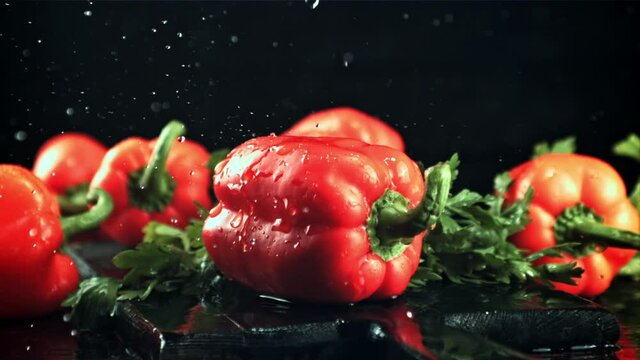 Drops of water with splashes fall on the sweet pepper. On a black background. Filmed is slow motion 1000 fps.