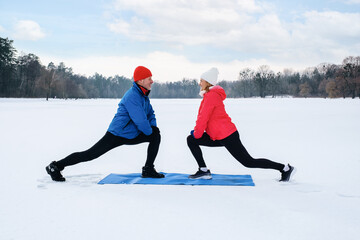 Fototapeta na wymiar Smiling senior couple warming before warms up and does stretching before workout on snowy winter lake. Elderly wife and husband doing fitness outdoors. Active lifestyle concept.