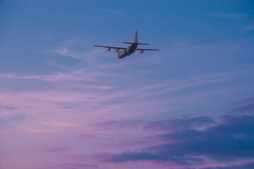 Fototapeta na wymiar British RAF Hercules C-130J military air-to-air refuelling aircraft in flight, illuminated by a pink sky sunset