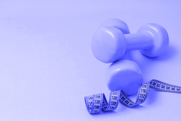 Light purple dumbbells with a centimeter ribbon on the background of the color very peri, copy space. The concept of fitness, healthy lifestyle, sports, weight loss, overweight.