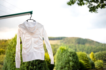Laundry drying outsite in front of a natural background. Clean white sport jacket hanging on a black laundry hanger. Making housework.