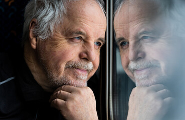 Senior man watching out of the window, reflection in the window, smilling concept