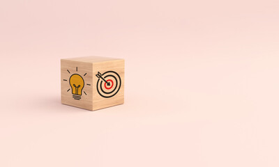 Wooden cube block with icon target and light bulb on pink background. Concept of business strategy.