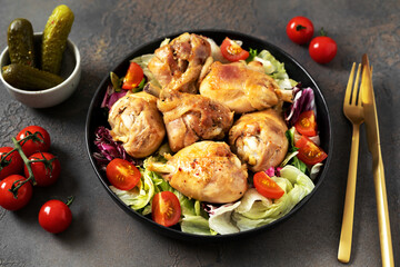 Fried chicken legs with salad in a plate on a dark kitchen table. Cooked poultry meat, pickles and tomatoes on the culinary background of closeup	