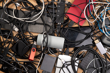 Tangled cables, hard drives and other electronic equipment on wooden desk, top view 