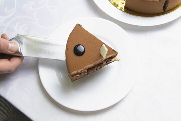On the festive table with a white tablecloth there is a chocolate cake, which is cut with a knife by a man.