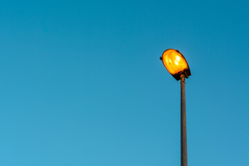 Street lantern, electric lighting. Glowing lamp on background of blue sky.