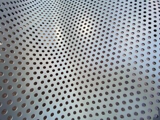 Pattern of holes in stainless steel lit with daylight, creating abstract background suitable for text and graphics