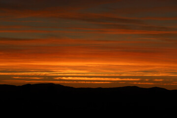 horizonte de nubes rojas y naranjas con puesta del sol y siluetas de montañas