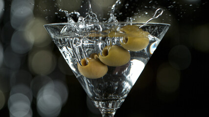 Martini with green olives splashing, close-up.