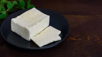 Large piece of feta cheese on dark wooden table. Selective focus
