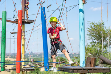 A sports boy overcomes obstacles on a rope road in an extreme park.
