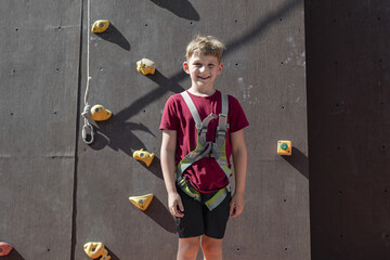 Joyful boy after overcoming obstacles on the climbing wall in sports park climbing wall.