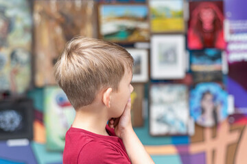 A boy in an art gallery looks at the paintings in the exhibition hall with attention.