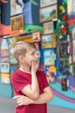A boy in an art gallery looks at the paintings in the exhibition hall with attention.