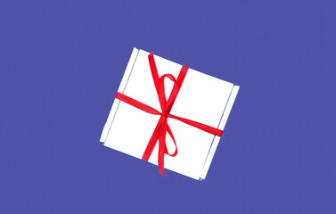 Gift with a red ribbon on a lilac background. Color of the year 2022. PANTONE 17-3938 Very Peri