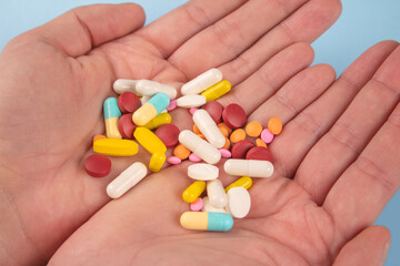 Man holding assorted multicolored medicine pills, capsules and tablets in his hands. A handful of pills. Immune system vitamins and supplemets. Dietary bio supplements