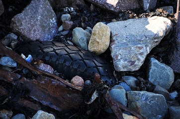 Rusty scrap metal and rubber tire on the beach. Seaweeds and boulders.  Horizontal image.