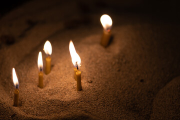 Scattered candles glowing with a golden yellow light in the sand, copy space