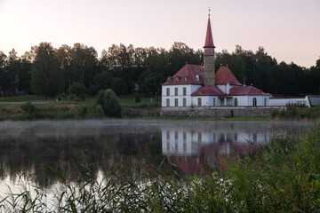 Prioratsky aka Priory palace in Gatchina stands on the shore of the pond. It is surrounded by a green forest. Small mansion, resembling a medieval 18th century European monastery with red tall spires.