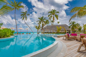 Amazing outdoor tourism landscape. Luxurious beach resort with swimming pool seaside beach chairs or loungers under umbrellas with palm trees and blue sky. Summer travel hotel and vacation background 