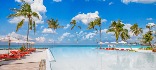 Amazing outdoor tourism landscape. Luxurious beach resort with swimming pool seaside beach chairs or loungers under umbrellas with palm trees and blue sky. Summer travel hotel and vacation background 