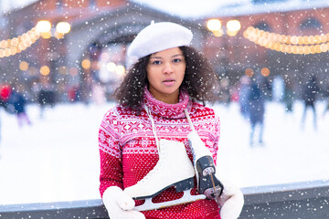 Close-up, pensive African American girl on the ice skating rink for a walk in winter. The portrait froze, young. Dark-skinned black woman with curly skates.