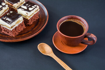 A cup of coffee on a dark table and pieces of delicious chocolate cake with cream and chocolate fondant on a plate