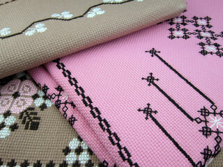    cross stitched flowers on pink and beige fabric background close-up             