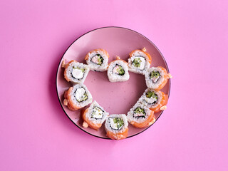 Sushi set in the shape of a heart on pink background. Valentine day or March 8th food concept.The concept of a romantic dinner at a sushi bar for February 14th.  